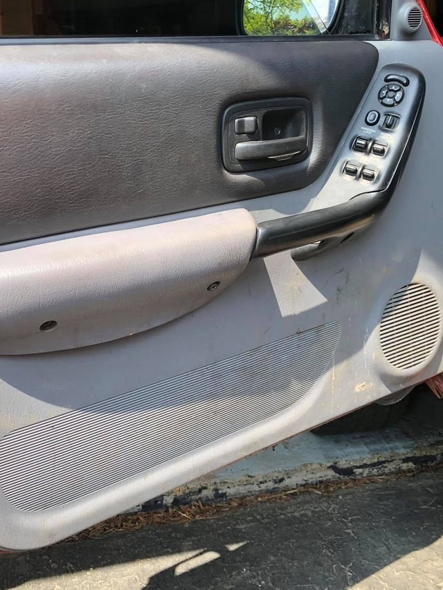 Driver door panel before the interior detail — the grey trim is dulled and streaked with grime around the armrest and speaker grille.