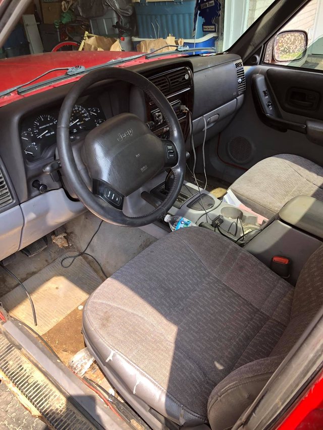 Driver area of a red SUV before the interior detail — soiled cloth seat, dirt and debris across the carpet and door sill, and a dusty dash.