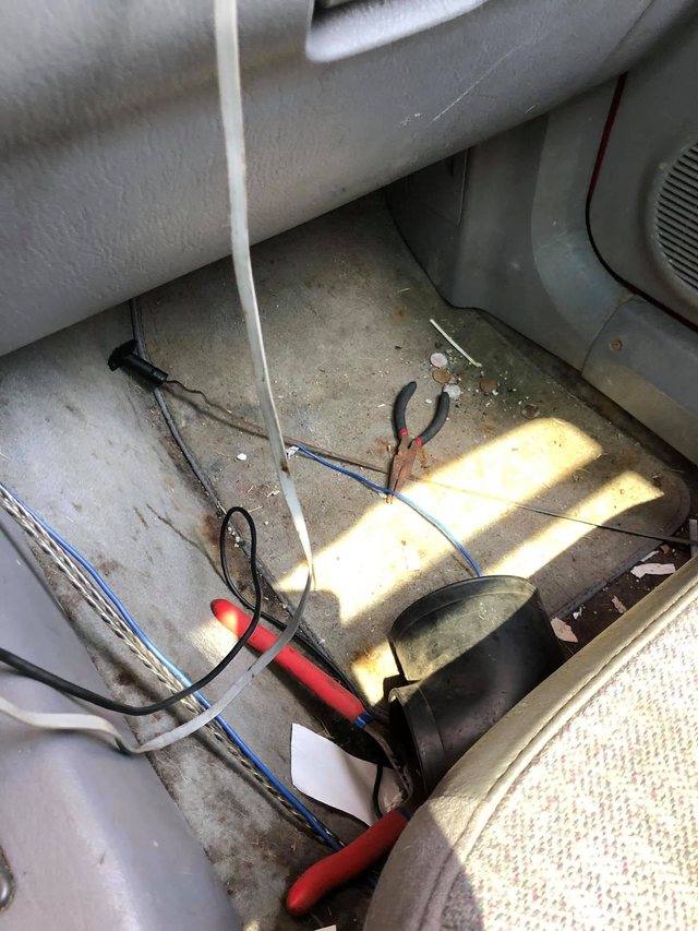 Passenger footwell before cleaning — the carpet is heavily soiled, with a work light and hand tools set down in the footwell.