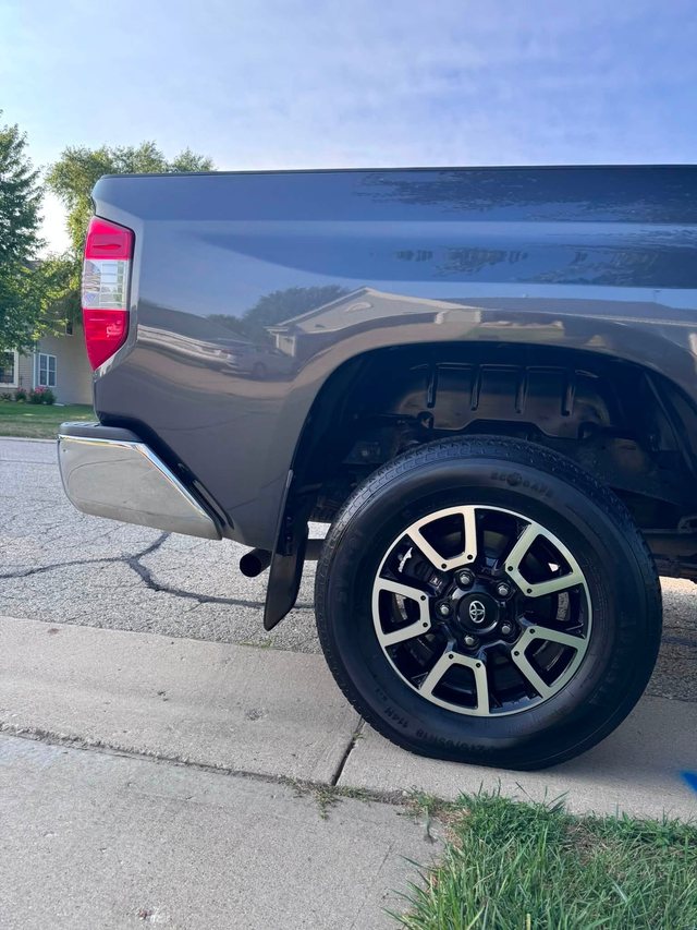 The same pickup rear quarter after detailing — the paint is glossy enough to reflect the house and trees, and the wheel face and tyre are clean.