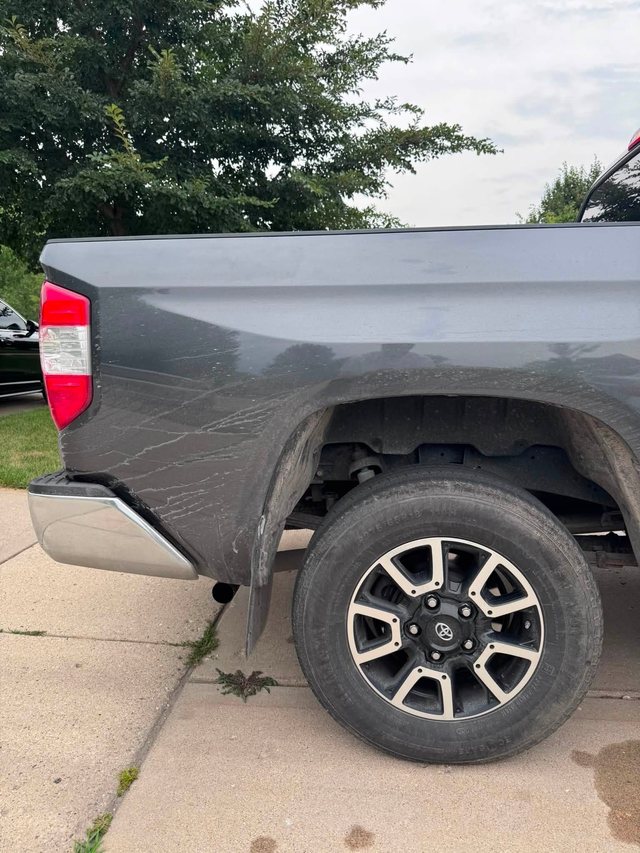 Rear quarter panel and wheel of a grey pickup before detailing — paint dulled by dried dirt streaks and the wheel coated in grime.